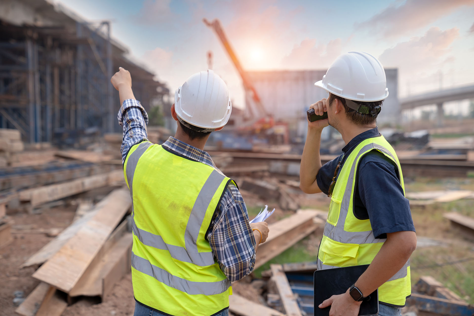 Construction and Temporary Works Solutions this image shows an active construction site with two people in PPE with their backs, one is pointing at the works and the other is communicating over radio
